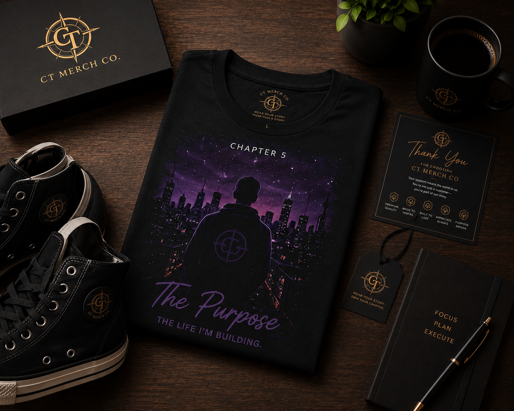 Flat lay of the CT Merch Co Chapter 5 The Purpose black graphic T-shirt featuring a purple city skyline and hooded figure, styled with premium CT branded shoes, notebook, mug, gift box, thank you card, and hang tag on a wooden desk.